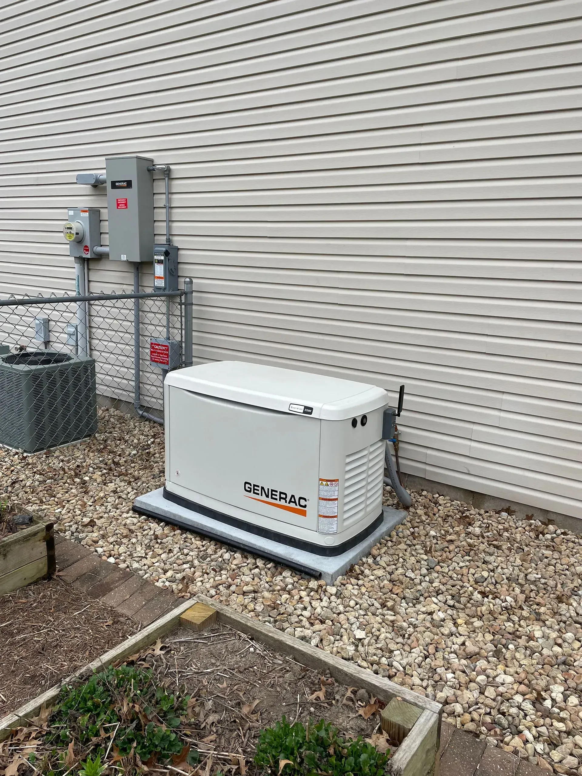 Outdoor standby generator beside a house, mounted on gravel near electrical equipment and siding.