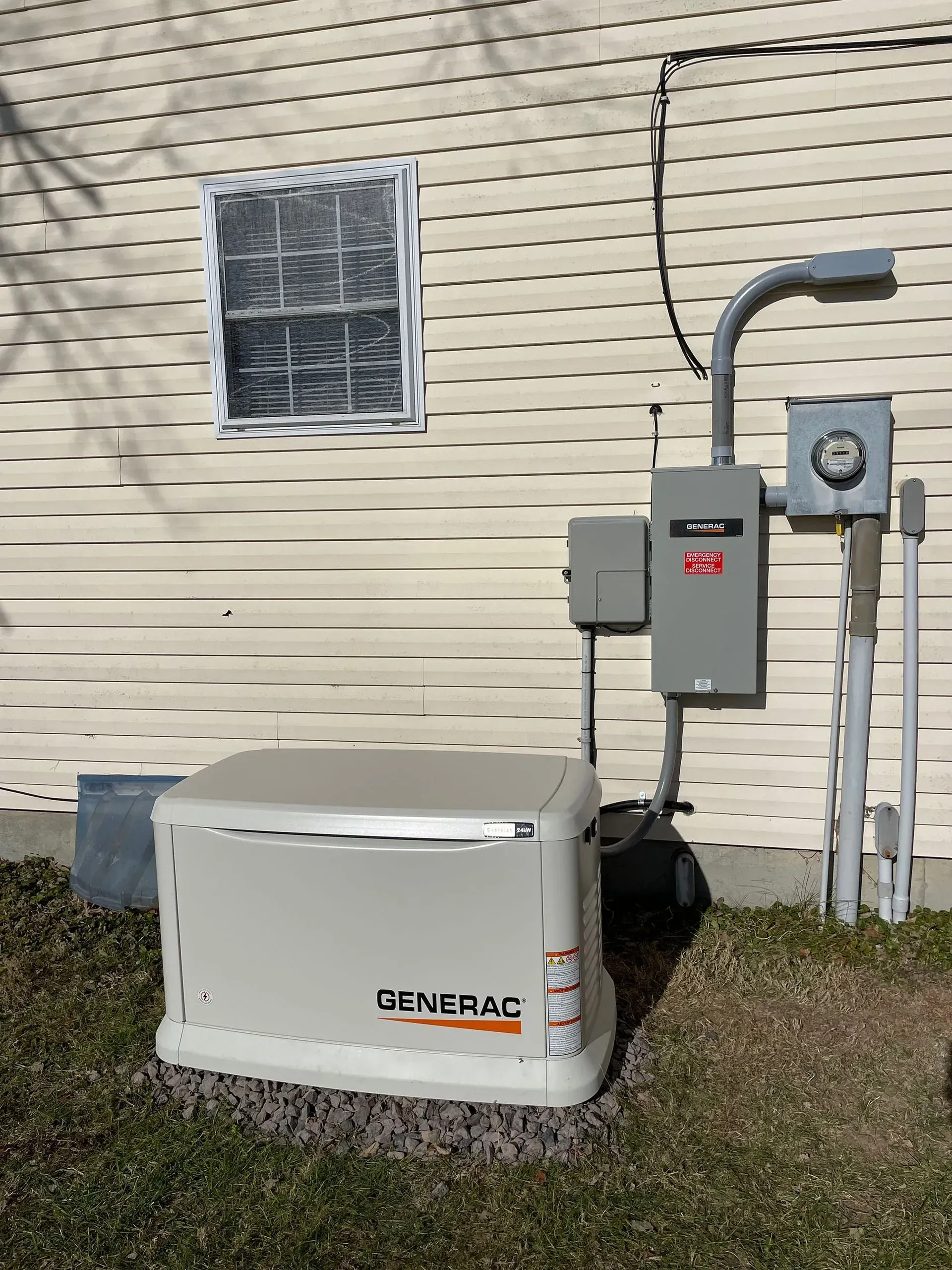 Outdoor generator beside house wall with electrical panels, meter, and conduit piping