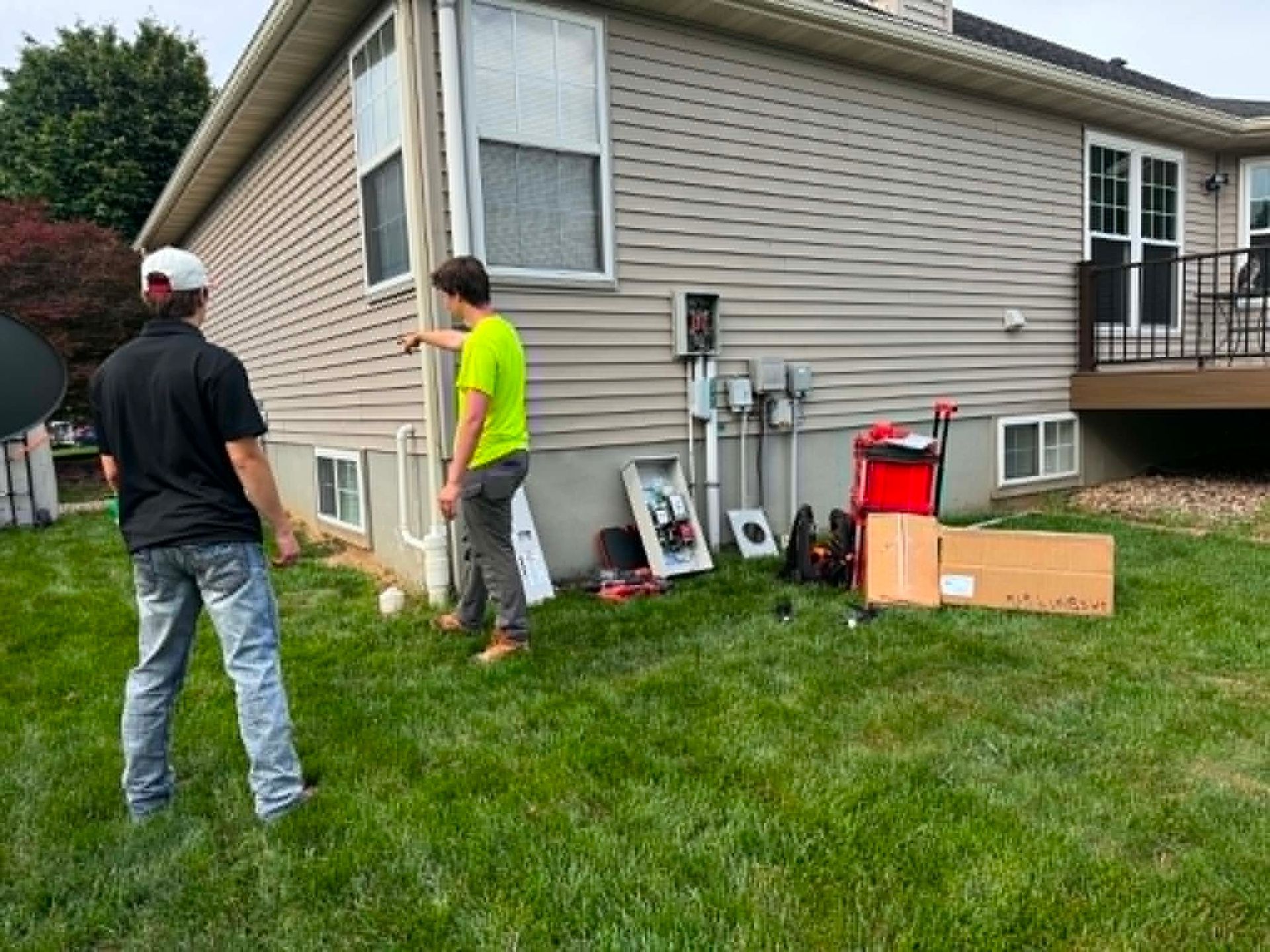 Two people inspecting the side of a house with tools and equipment on the lawn.