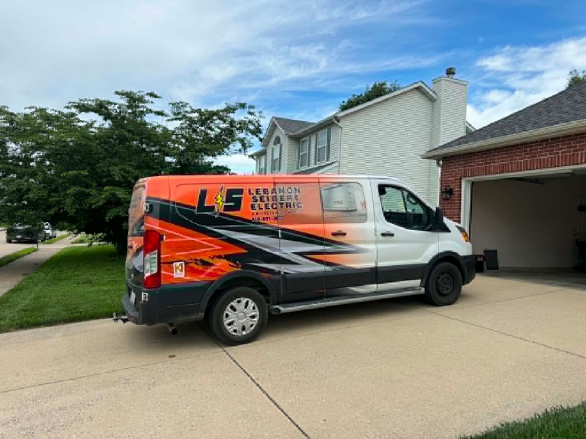 Orange and black work van parked in a suburban driveway beside a brick garage