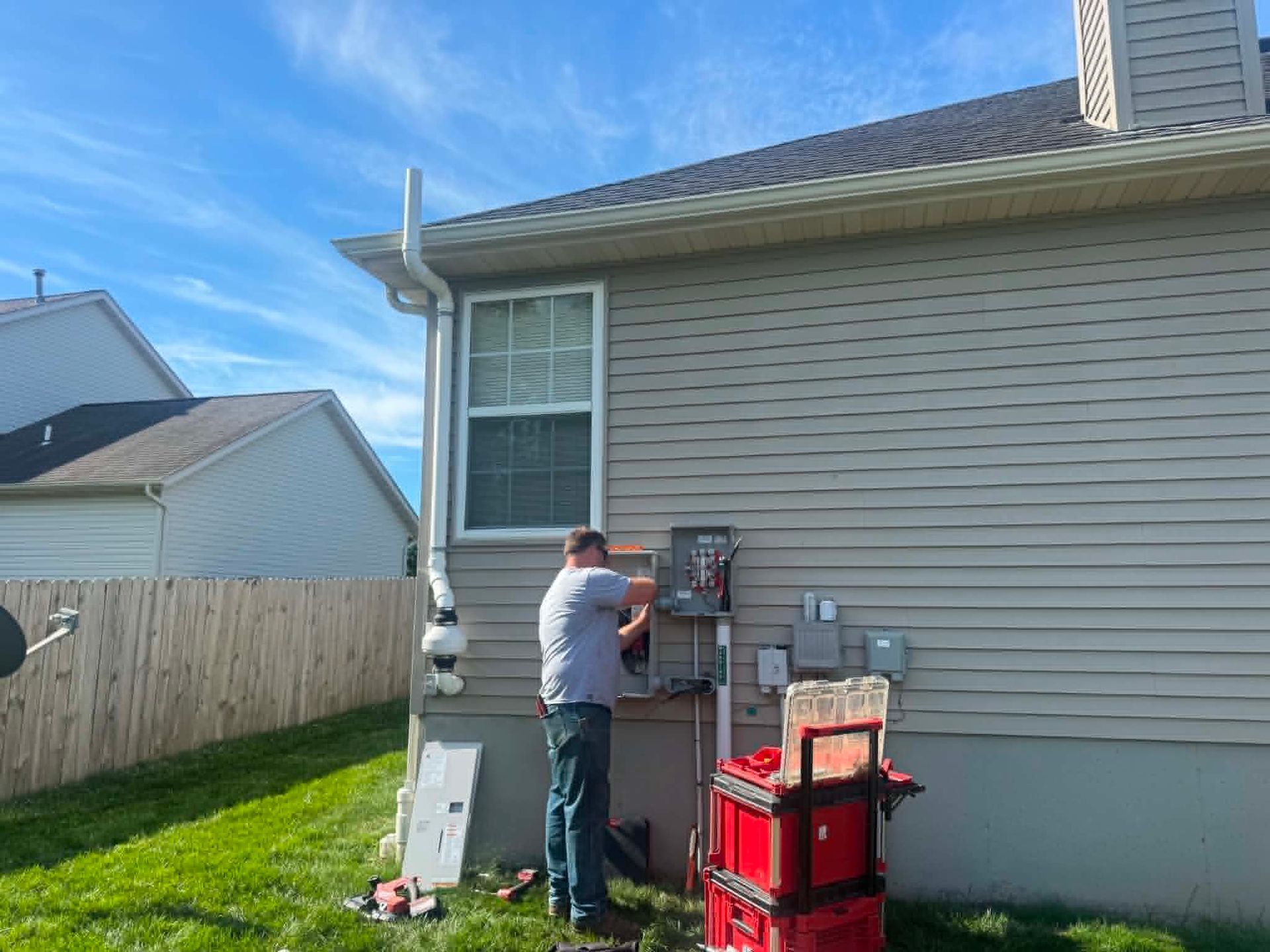 Person working at utility meters beside a beige house, with stacked red bins nearby.