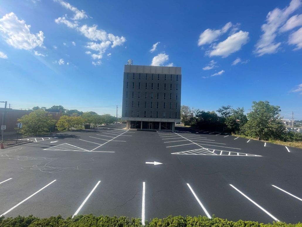 Asphalt road leading to a large white building with dark lettering; cloudy sky overhead.
