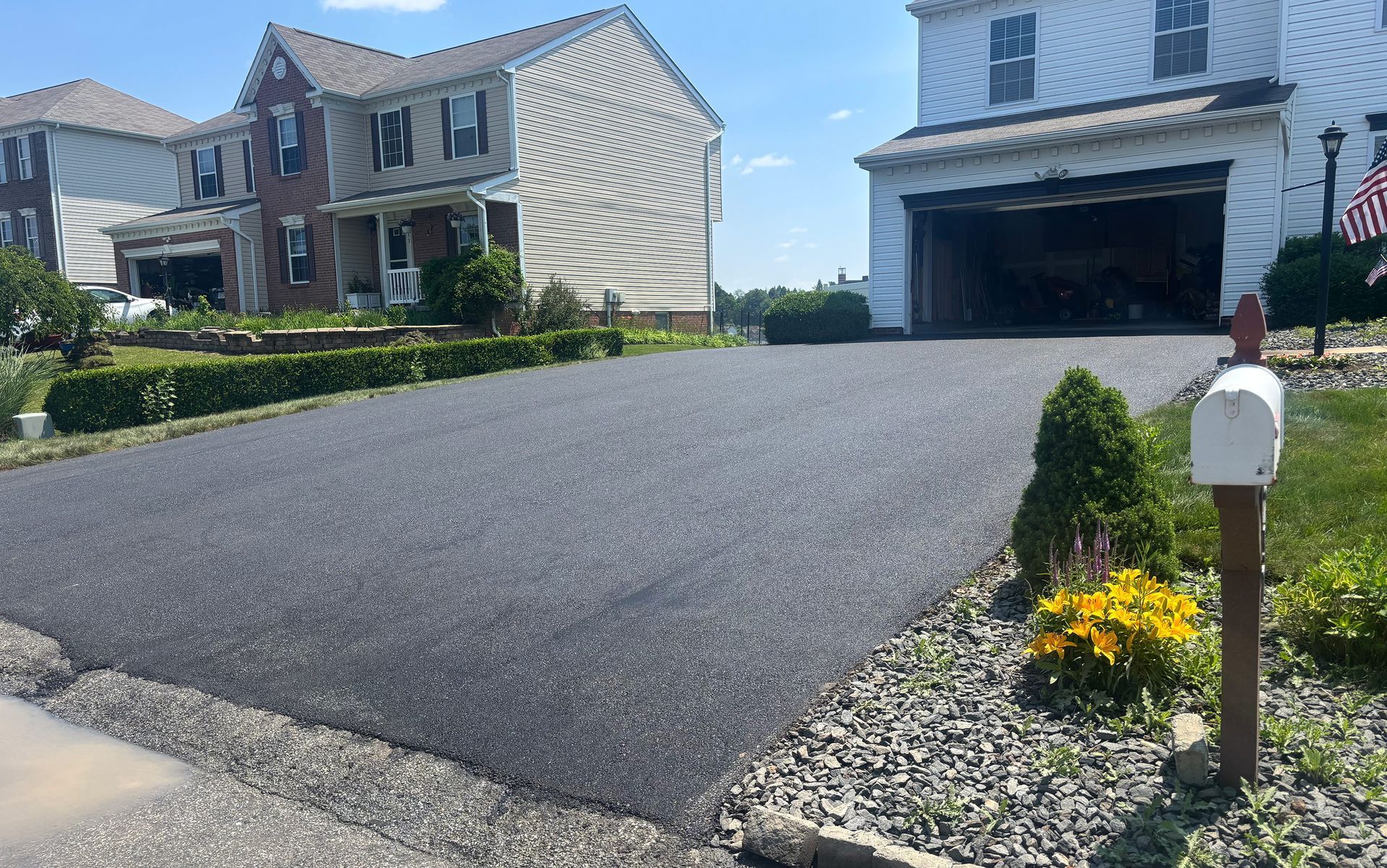 Black asphalt driveway in front of two-story houses; white garage door open. 
