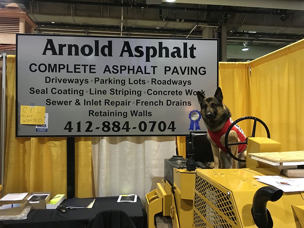 Sign for Arnold Asphalt company with a dog wearing a red vest near a yellow road roller.