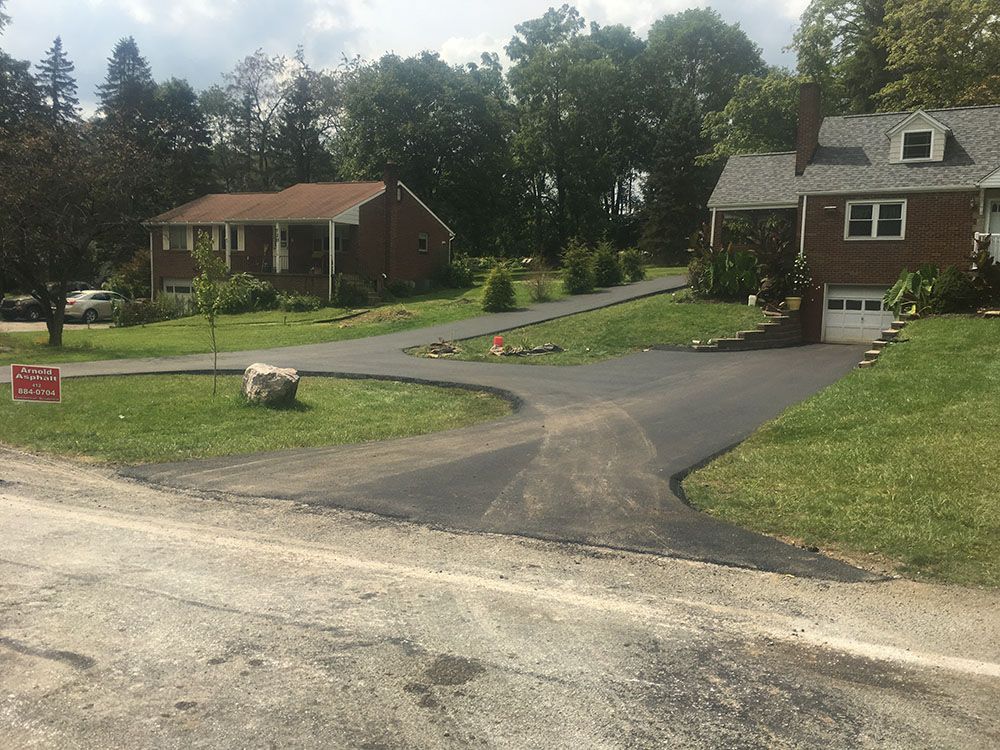 Asphalt driveways leading to two houses with green lawns and trees in the background.