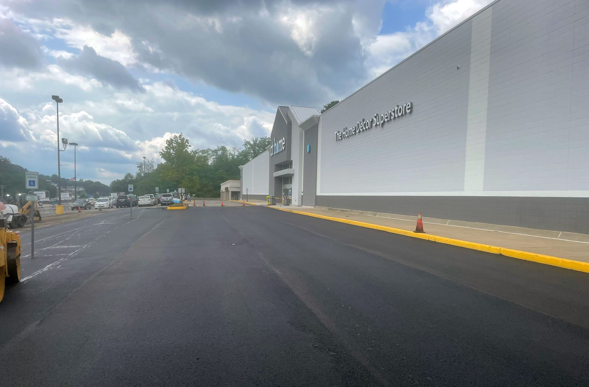 Freshly paved parking lot in front of a white retail store building with a partially cloudy sky above.  