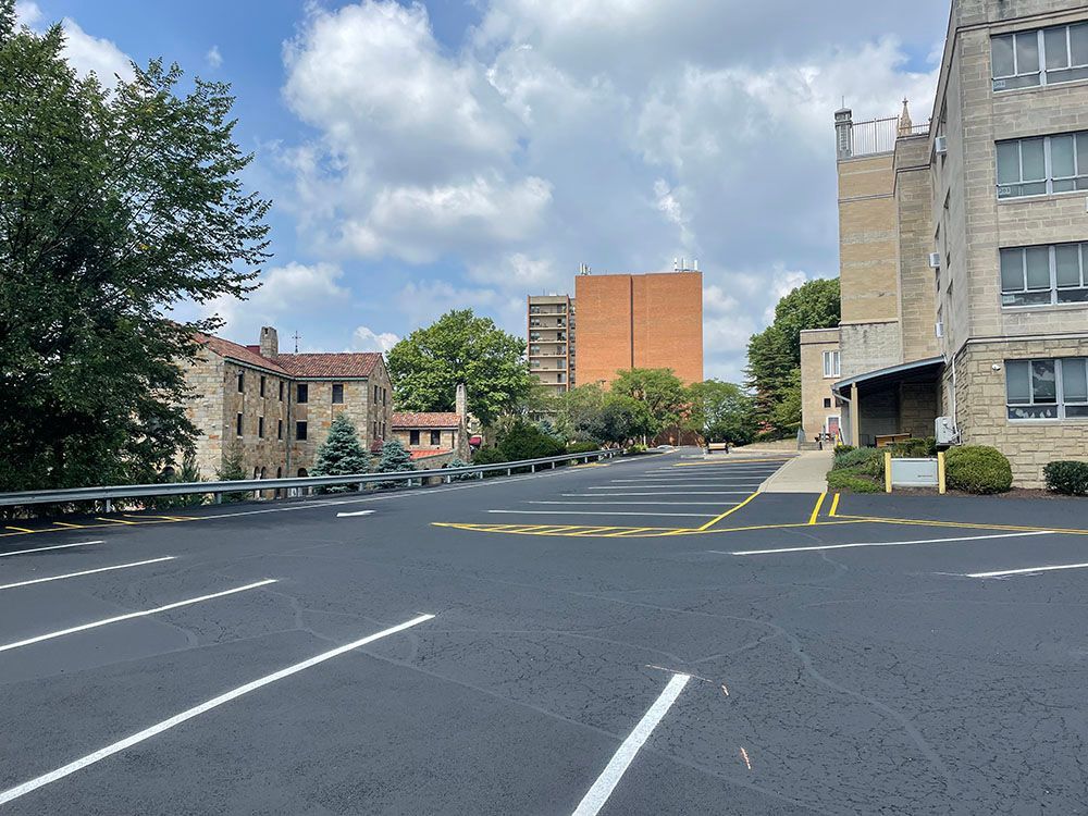 Empty parking lot with buildings and trees under a partly cloudy sky.