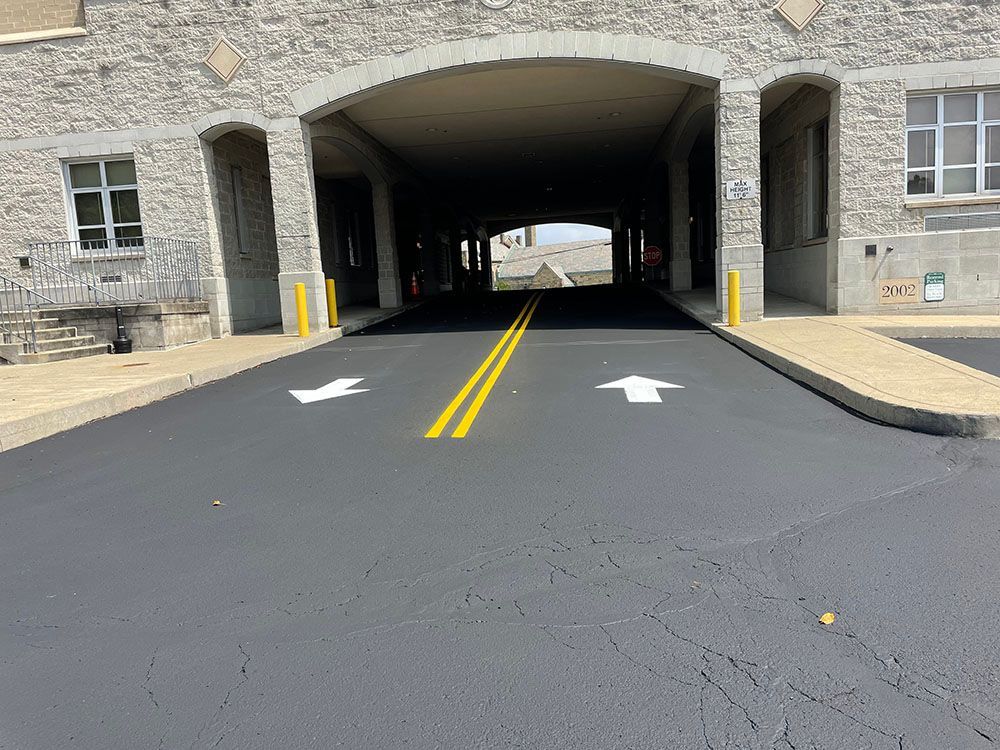 Asphalt road under an arched building entrance with yellow lines and white directional arrows.