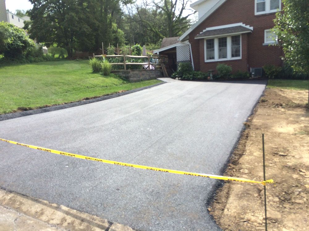 Newly paved asphalt driveway with a brick house in the background. Yellow caution tape across the driveway.