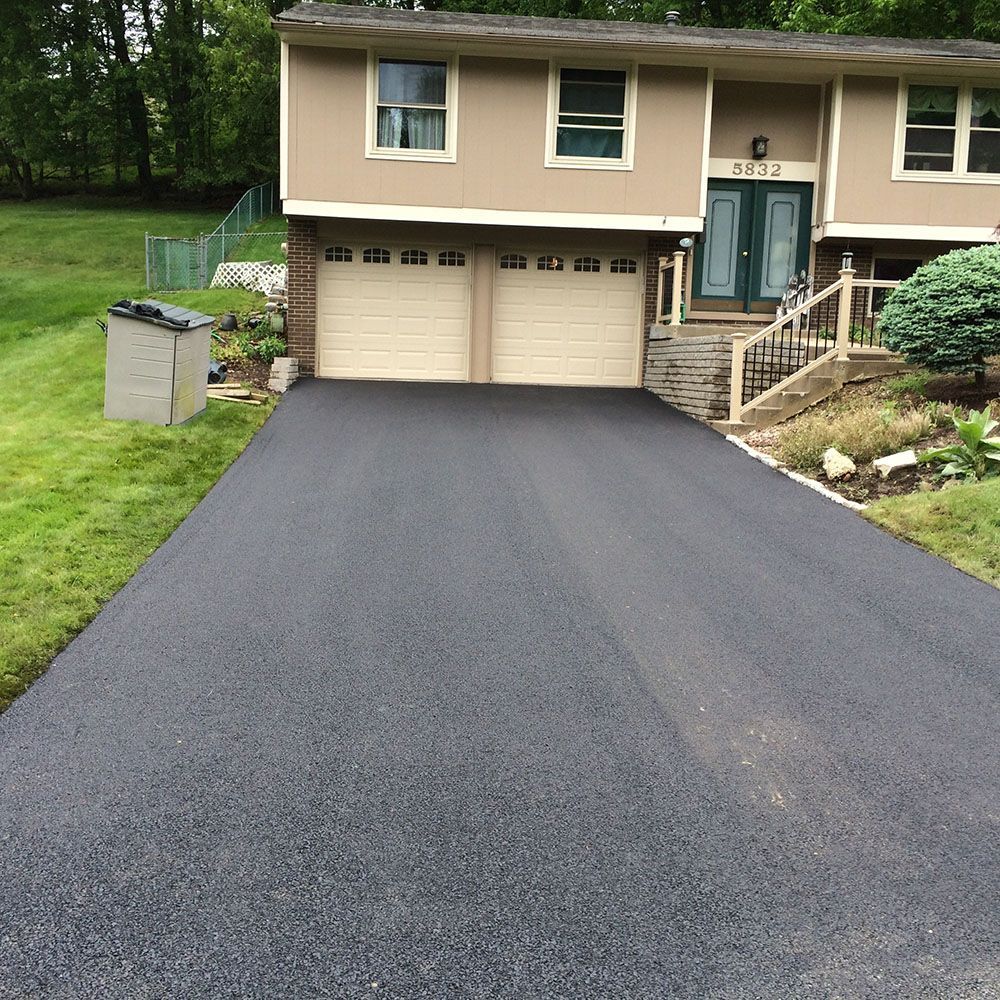 Black asphalt driveway leading to a two-car garage with tan doors, attached to a beige house.
