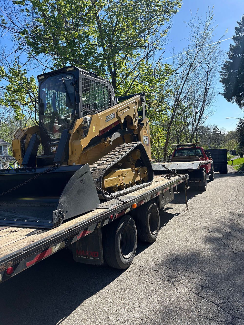 Yellow and black Caterpillar track loader on a flatbed trailer, pulled by a red truck on a sunny day.