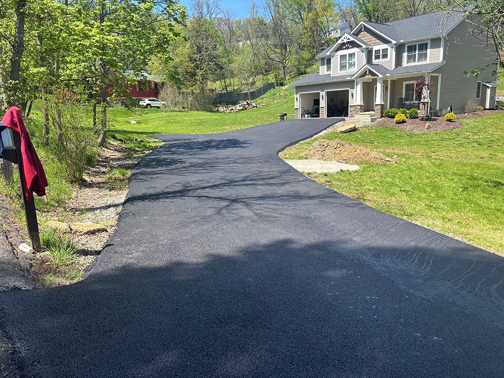 Newly paved asphalt driveway leading to a two-story house with a garage, on a sunny day.