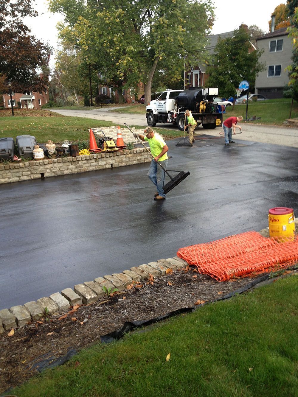 Asphalt paving in progress on a residential street. Workers in safety vests are using tools.