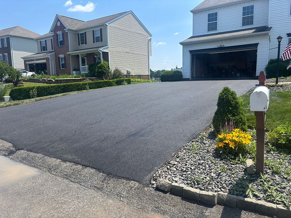 A newly paved black asphalt driveway leads to a suburban home with an open garage.