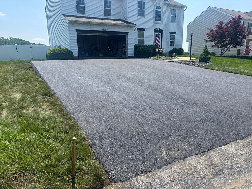 Newly paved asphalt driveway in front of a two-story house with a white exterior and a two-car garage.