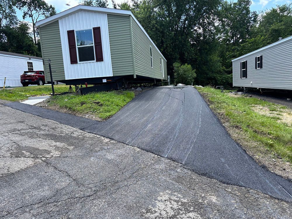 Mobile home on elevated foundation next to a newly paved asphalt driveway.