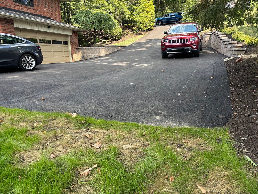 A red SUV on a newly paved asphalt driveway in front of a house, with a parked gray car to the left.