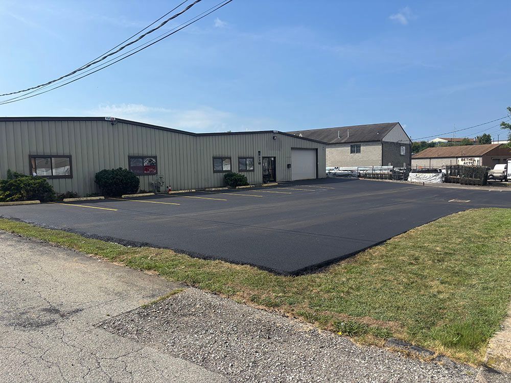 Exterior of a commercial building with paved parking area. Gray metal siding, several windows, and a garage door.