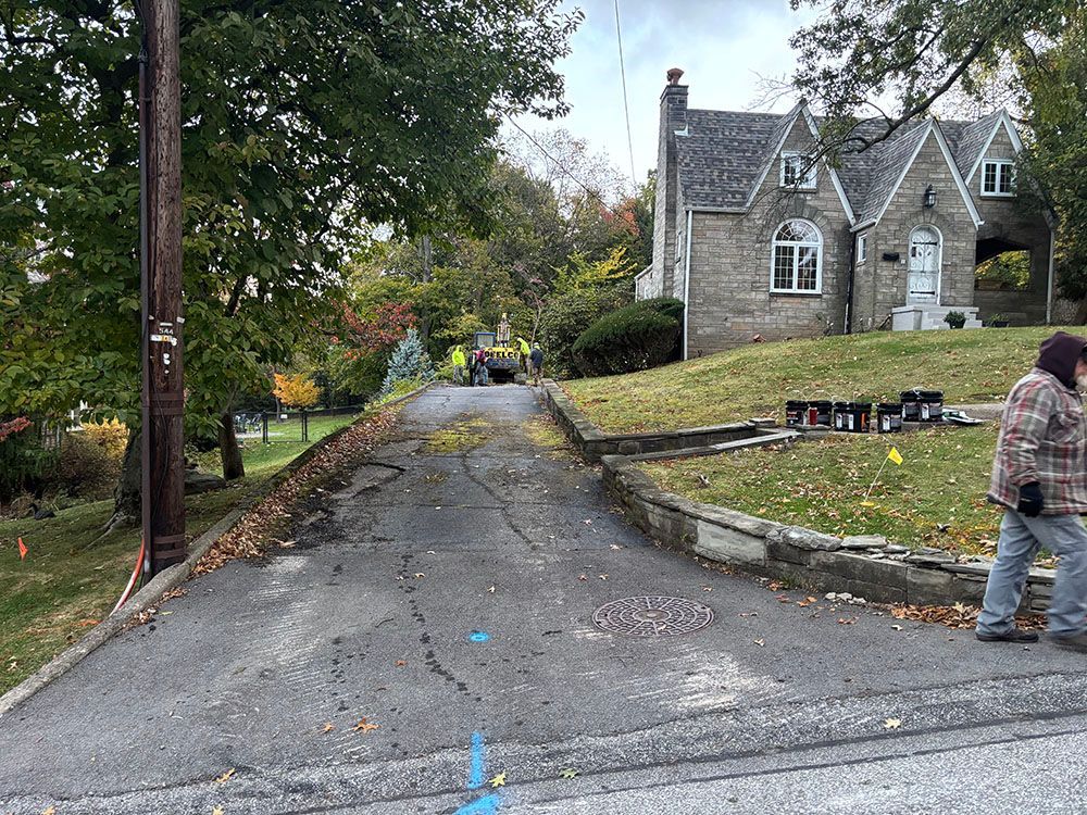 Asphalt driveway with construction equipment, stone house, worker walking.