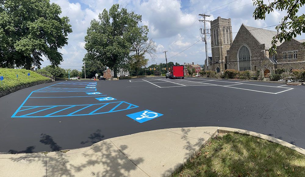 Newly paved parking lot with blue handicap spaces and a church in the background on a sunny day.