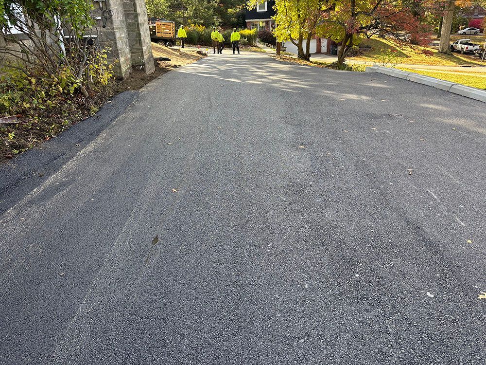 Newly paved asphalt road on a street, with workers and construction equipment visible in the background.