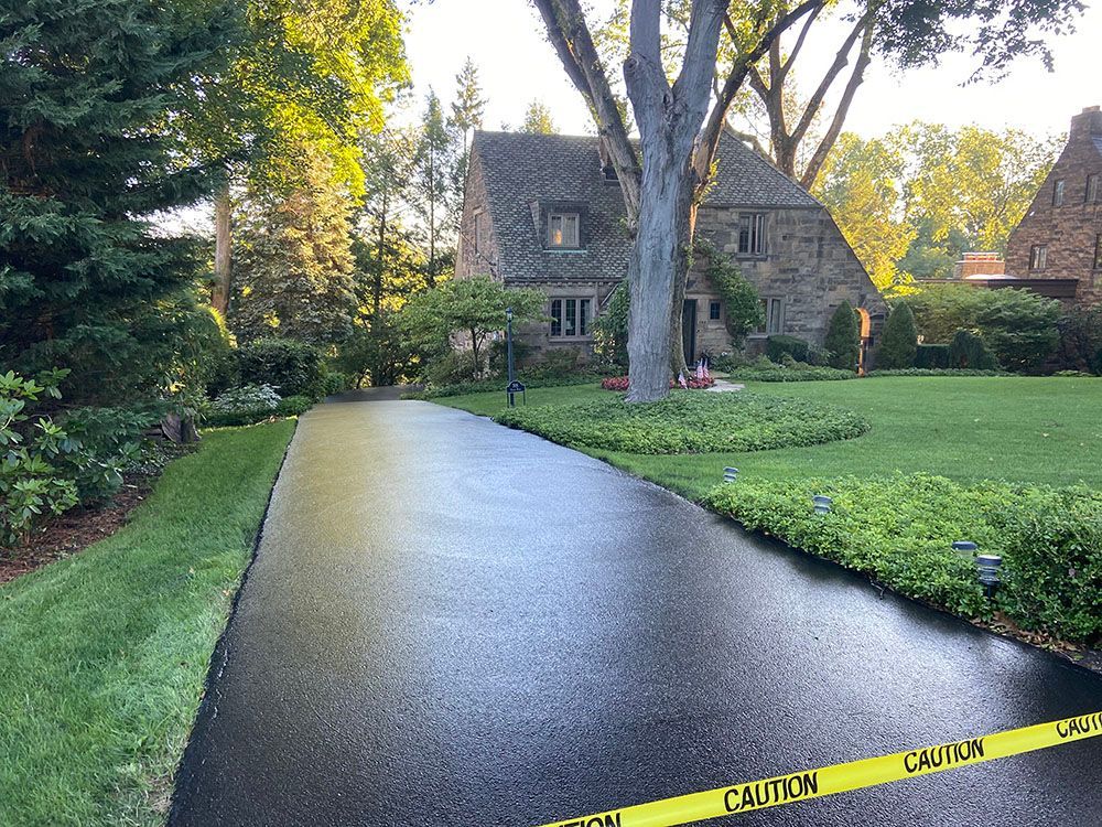 Newly paved asphalt driveway leading to a stone house.