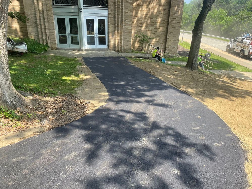 Asphalt pathway leading to a building entrance. People near the entrance and road.