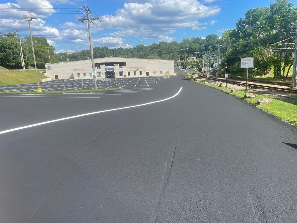 New asphalt road and parking lot with a building and train tracks in the background, blue sky.