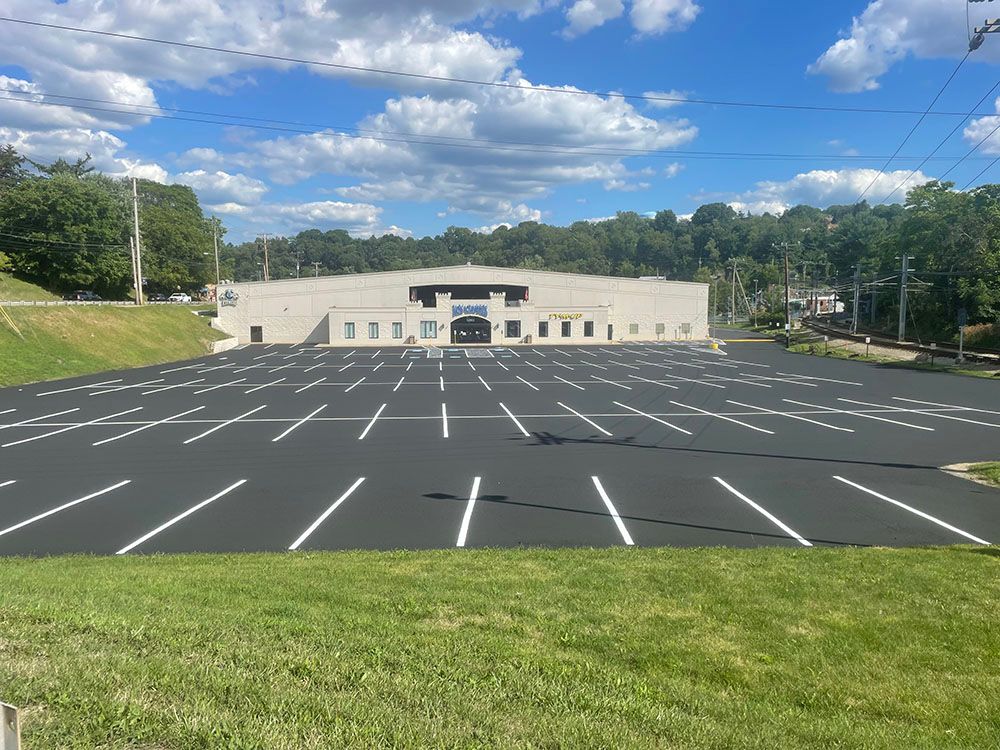 Large building with a massive empty parking lot; blue sky, white clouds; green grass in foreground.