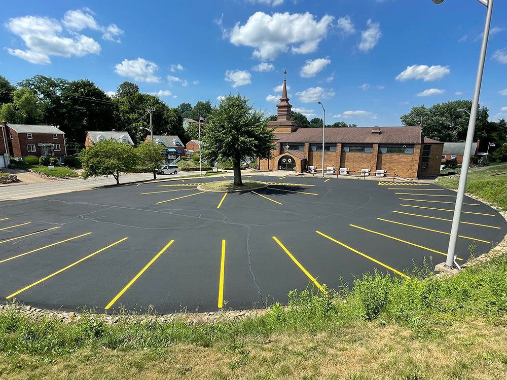 Newly paved asphalt parking lot with yellow lines, building in background, blue sky.