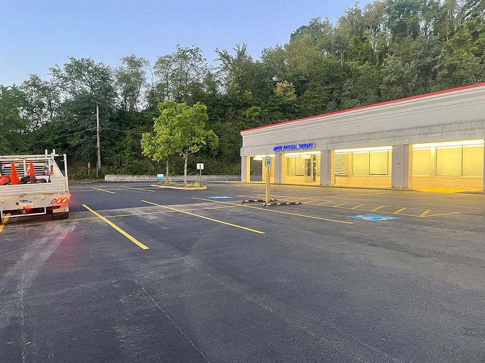 Newly paved parking lot with yellow lines, a truck, and a building.