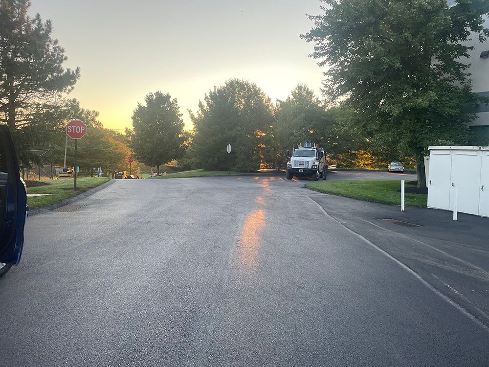 Wet asphalt road with sunlight reflecting, trees, and a garbage truck. Stop sign visible.