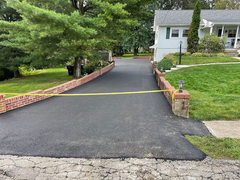 Black asphalt driveway with yellow caution tape, bordered by brick walls, leading to a house.