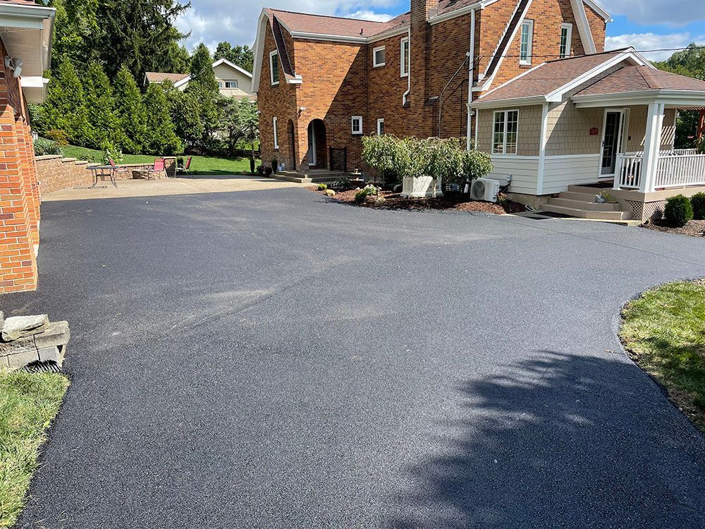 Newly paved asphalt driveway in front of a brick house with a white porch.