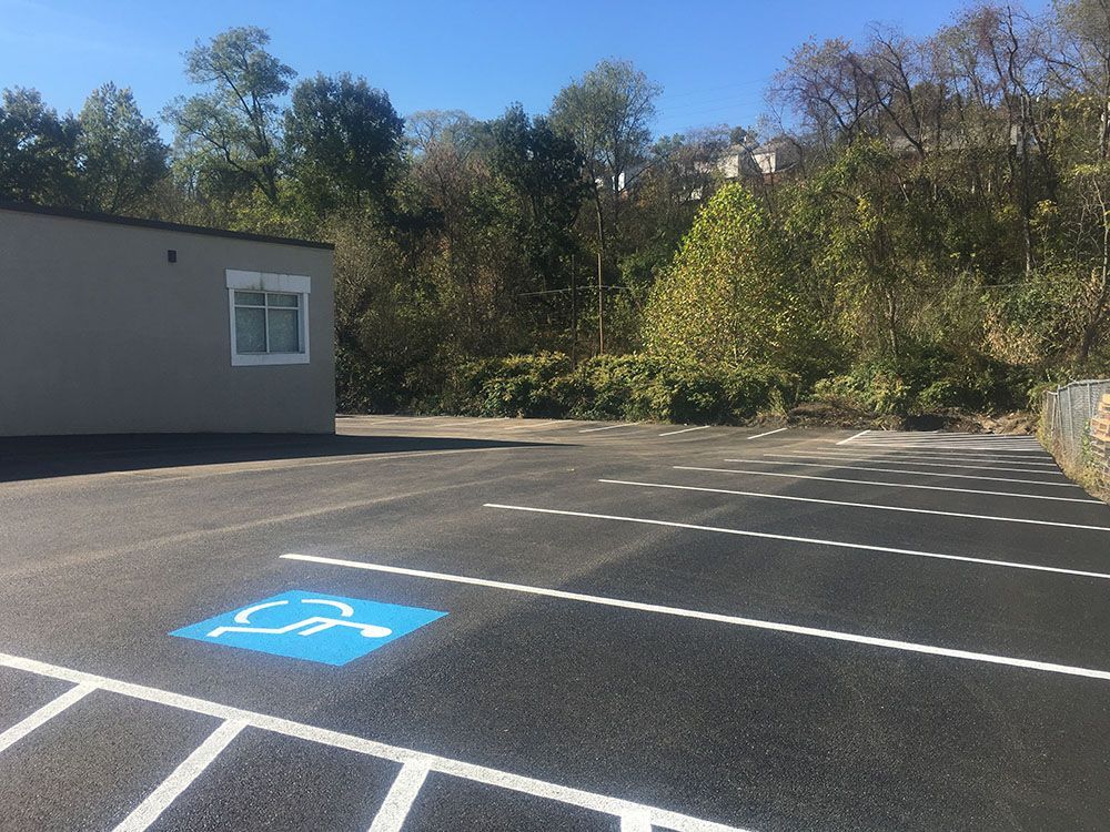 Parking lot with accessible parking space marked with blue wheelchair symbol; building and trees in background.