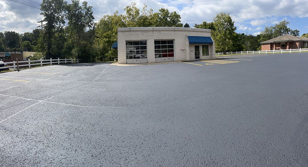 Paved parking lot in front of a small, white building with a blue awning.