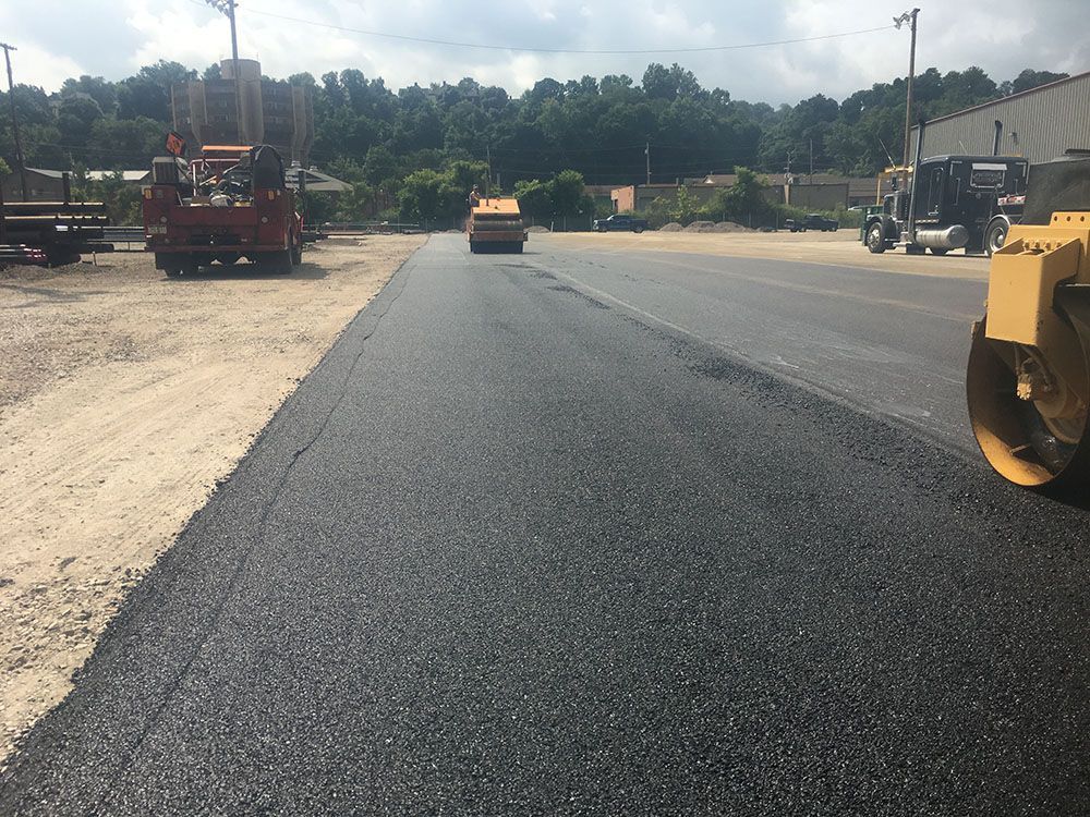 Asphalt paving in progress on a road, with construction vehicles in the background.