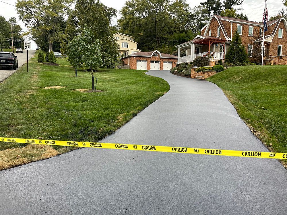 Freshly paved driveway with caution tape in front of a house, surrounded by green grass.