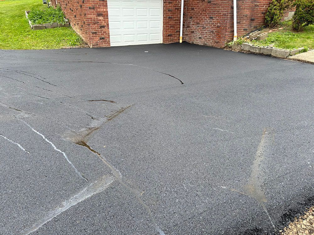 Asphalt driveway with cracks in front of a brick building with a garage door and small patches of green grass.