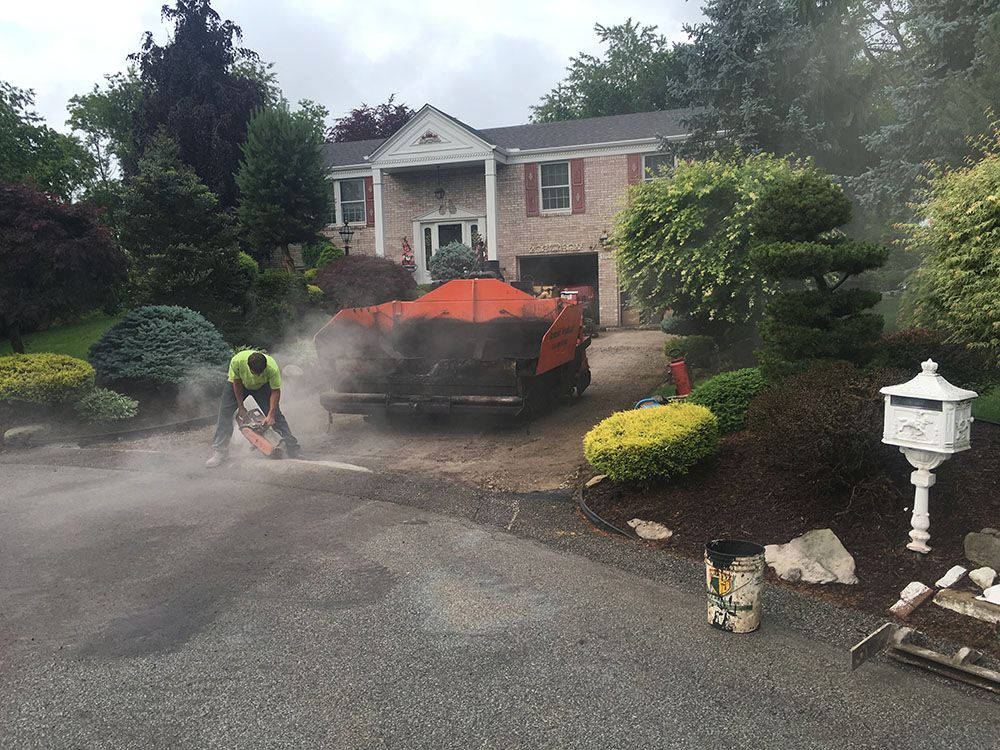 Person cutting asphalt driveway with a saw, asphalt paving truck, residential house.