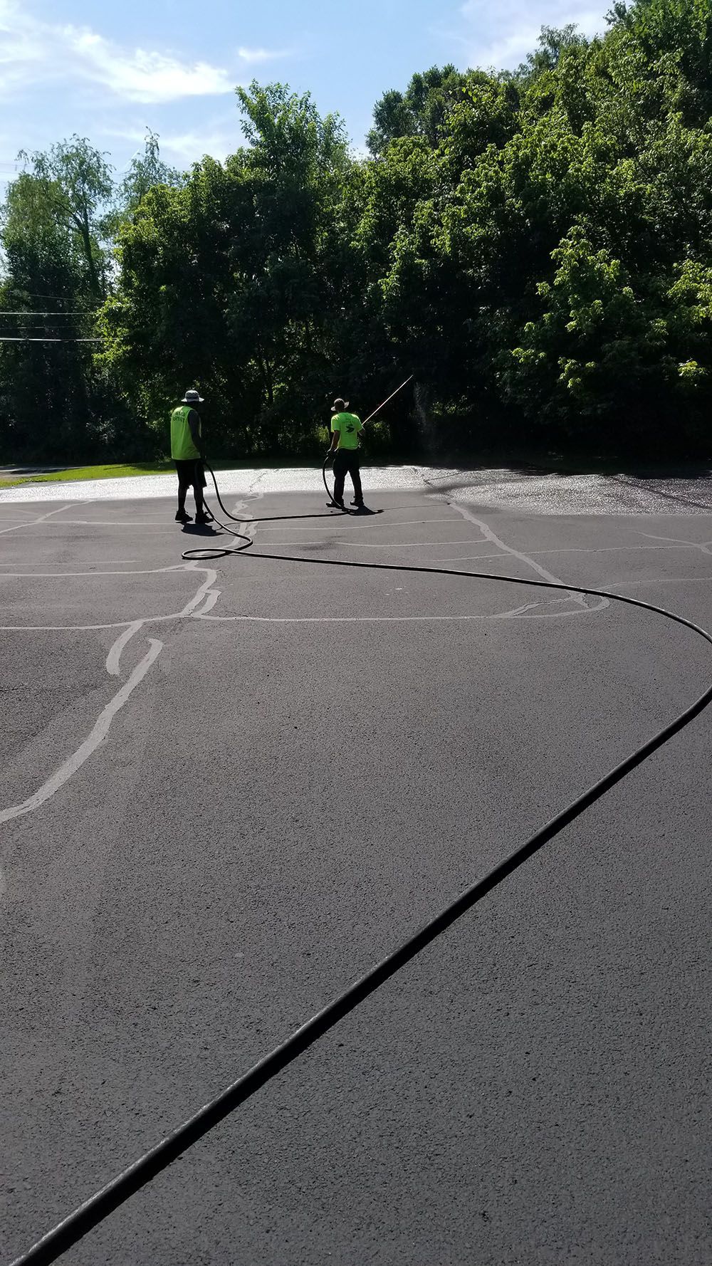 Two workers seal cracks in asphalt surface on a sunny day.