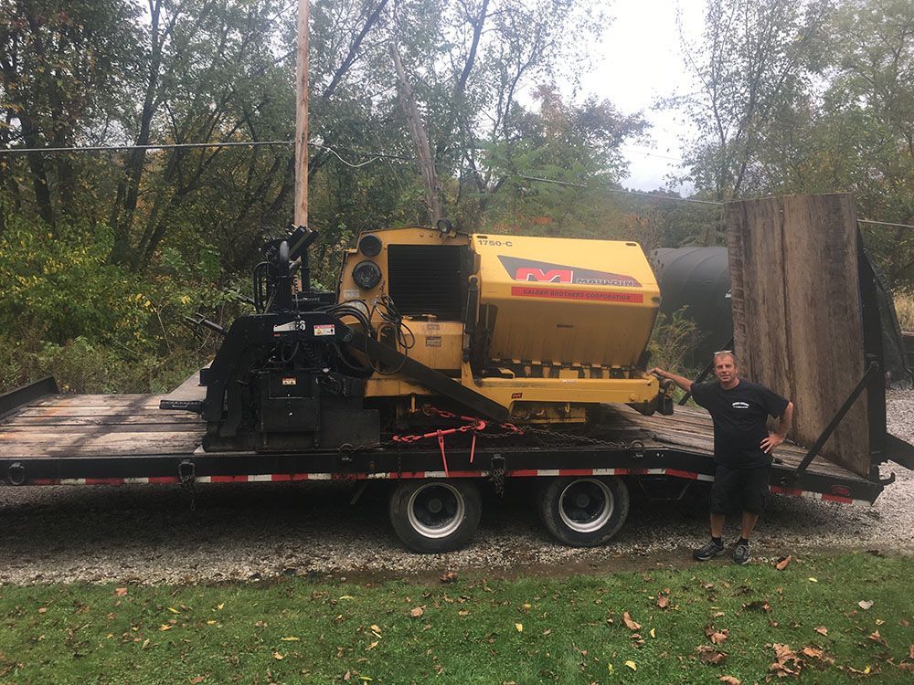 Man standing next to a yellow wood chipper on a trailer. Trees are in the background.