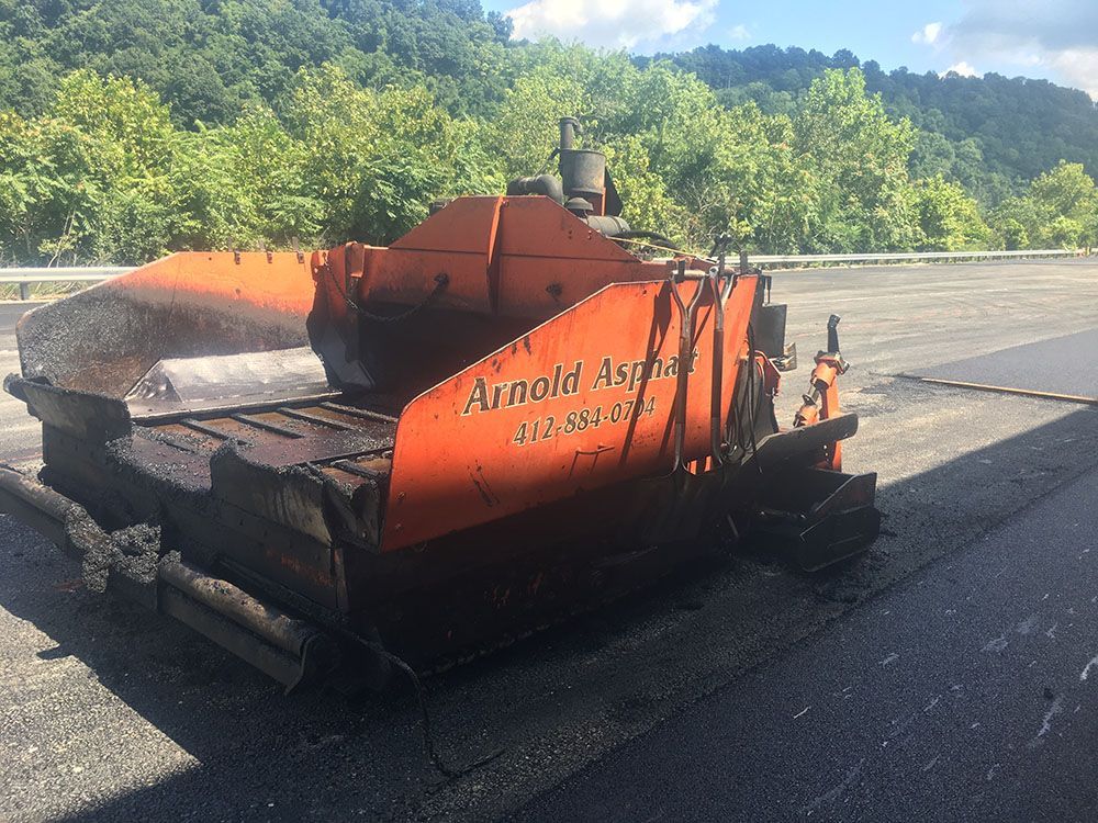 Orange asphalt paving machine laying new asphalt on a road.