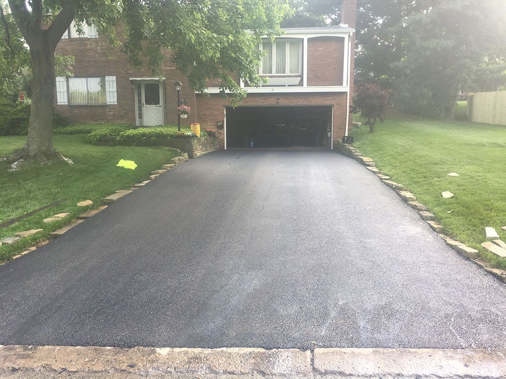 Newly paved asphalt driveway leading to a brick house with a garage.