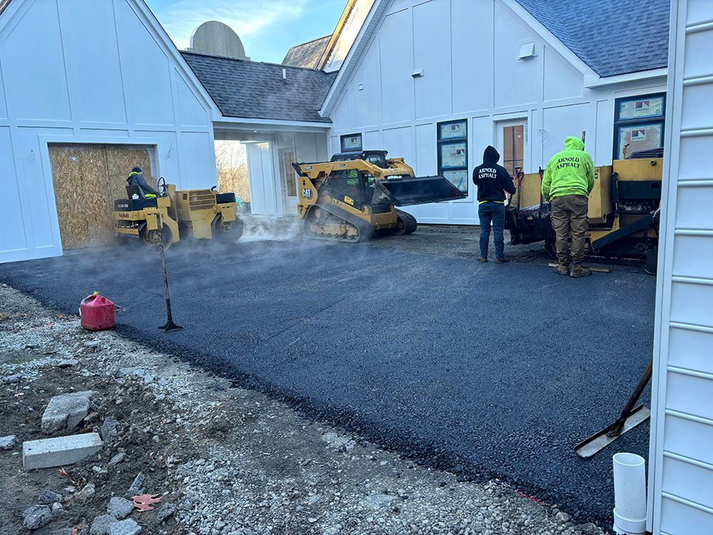 Asphalt paving a new driveway. Workers operate equipment near a building.