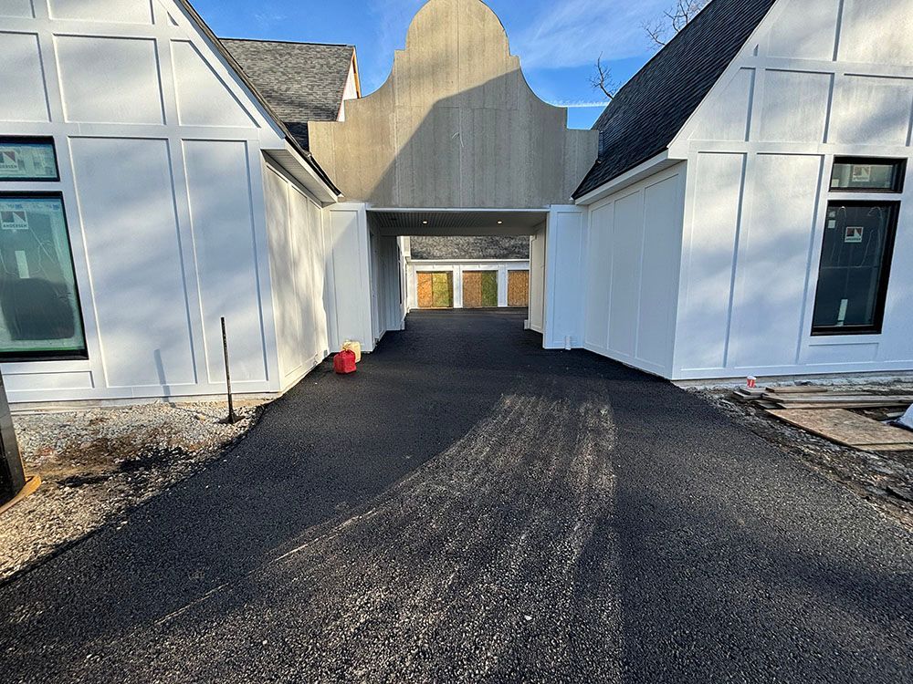 Black asphalt driveway leads through a white-paneled building with dark roof under a clear sky.