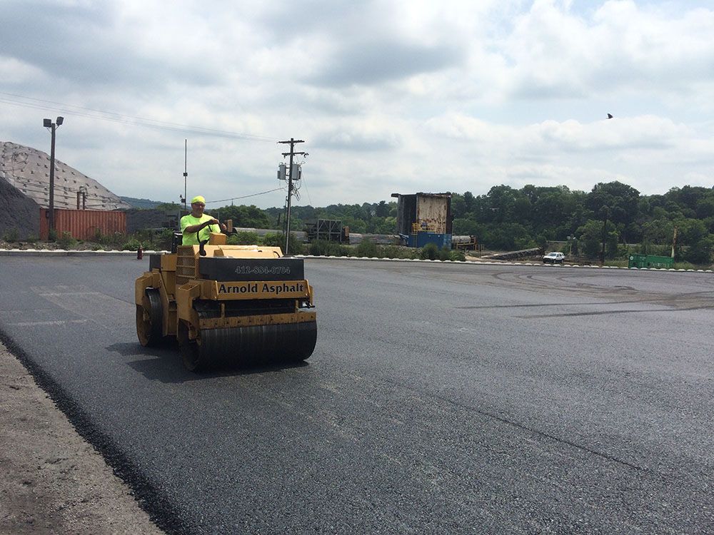 Worker operating a steamroller, compacting asphalt on a paved road.