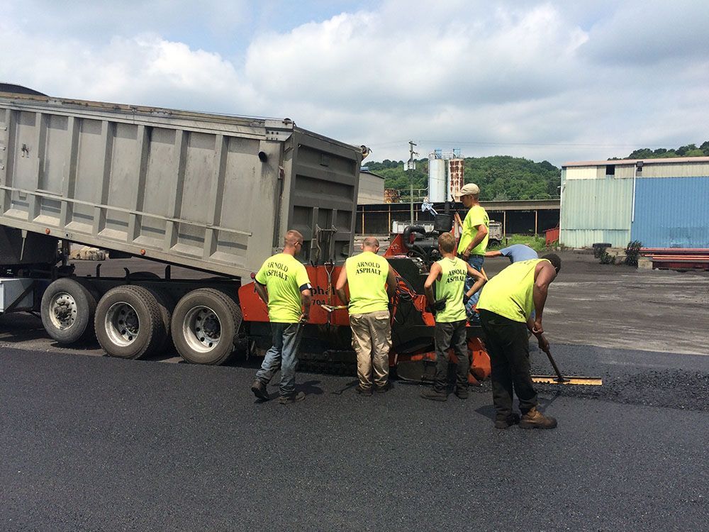 Road workers paving with asphalt, truck dumping asphalt into a machine, sunny day.