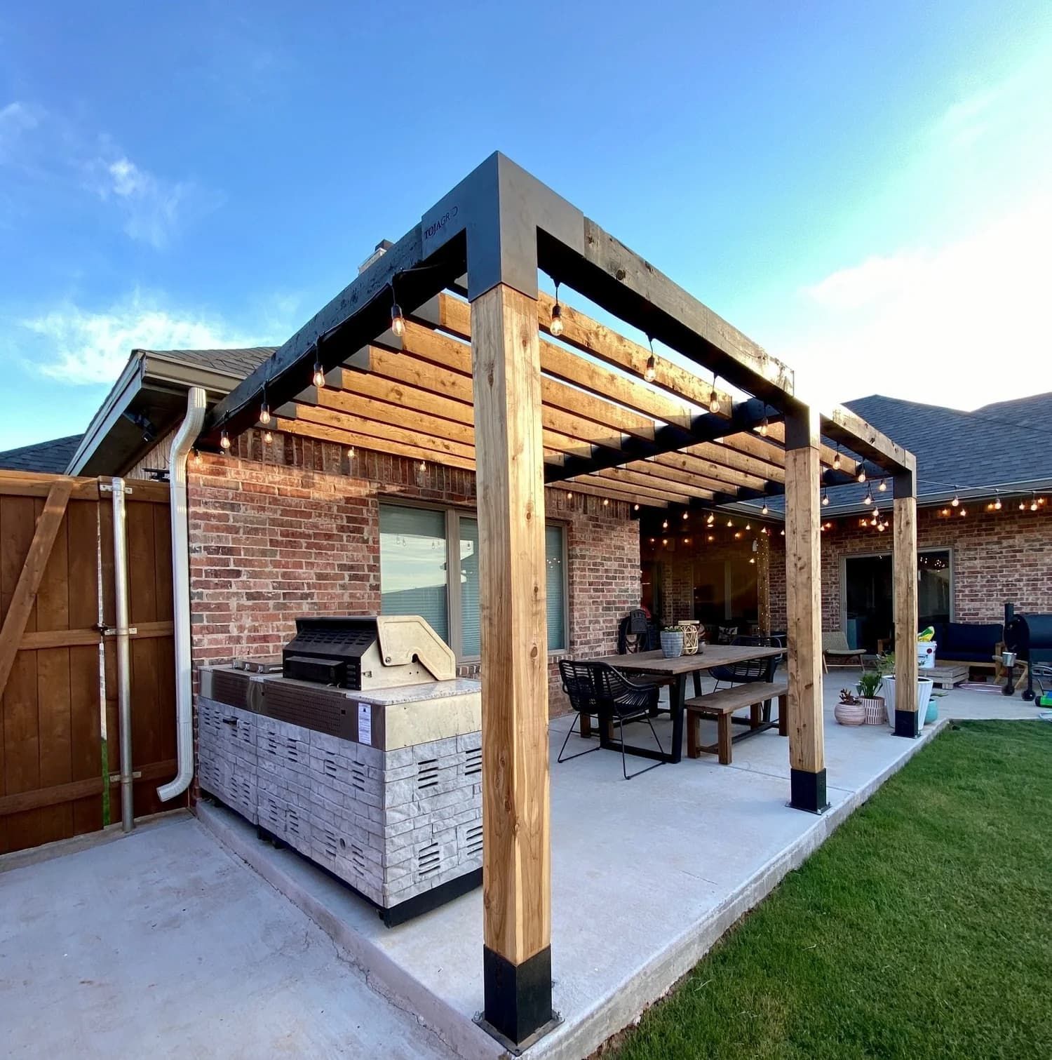 A patio with a pergola and a grill in front of a brick house.
