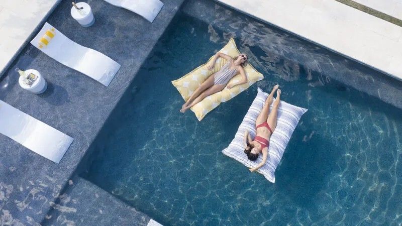 Two women are floating on rafts in a swimming pool.